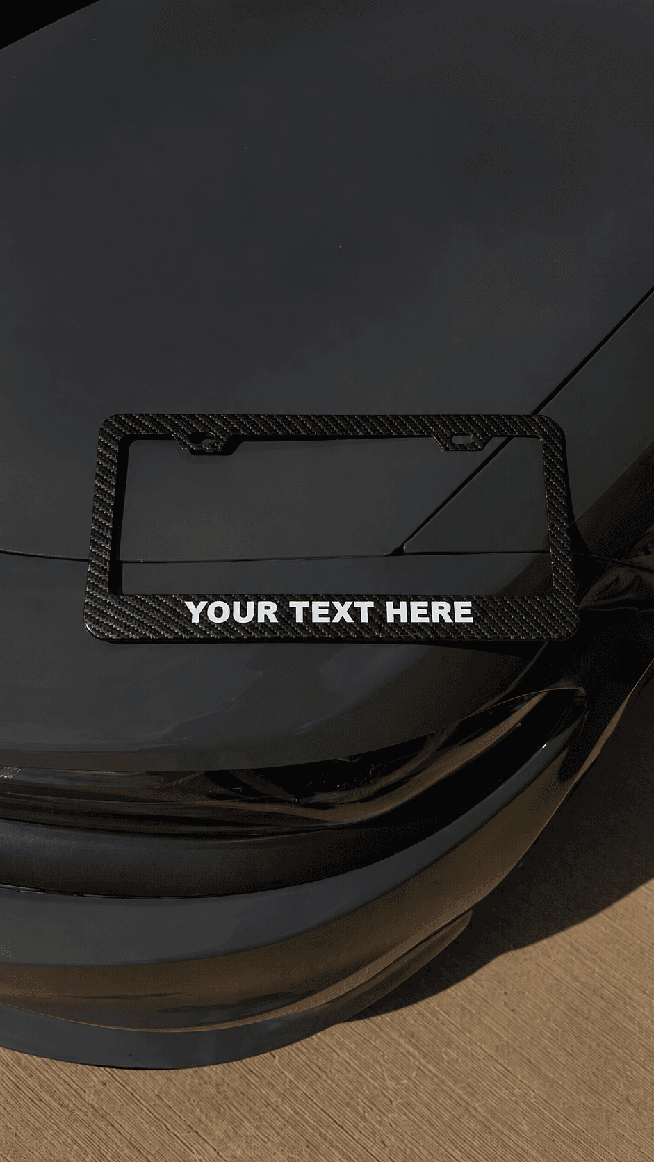 Carbon fiber license plate frame reading YOUR TEXT HERE on a car hood